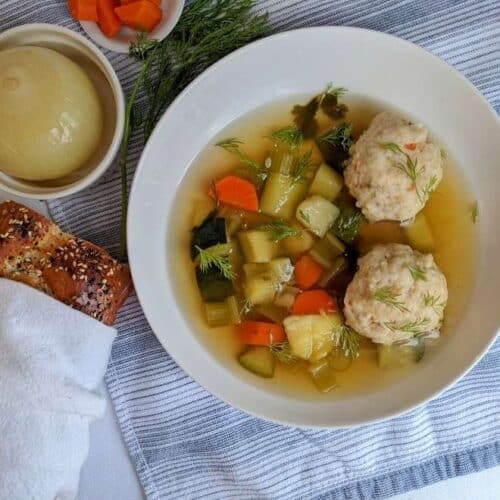 Matzo ball soup in a white bowl with challah