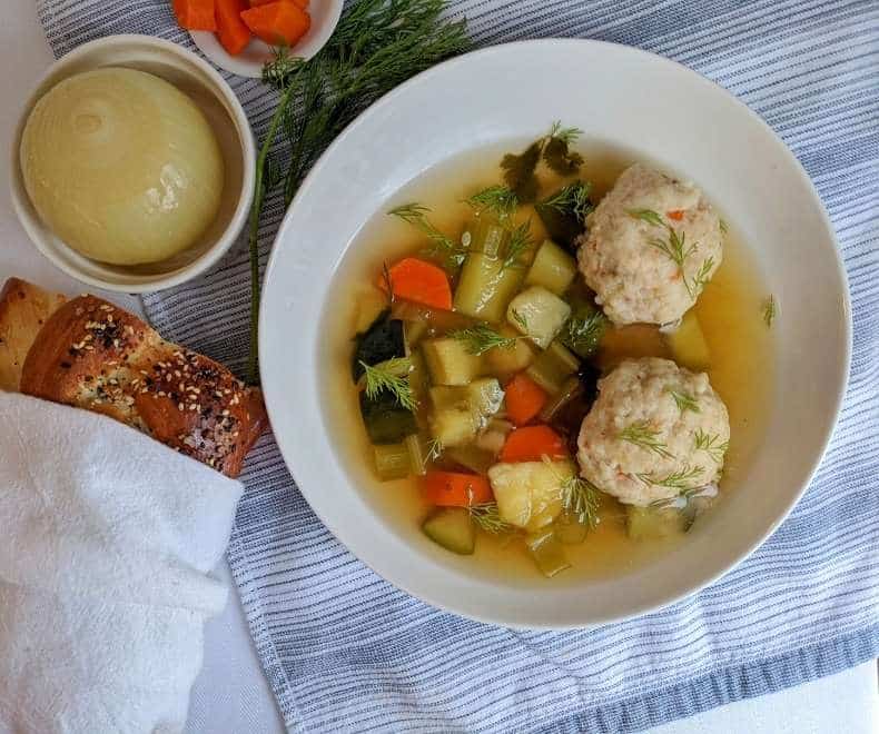Matzo ball soup in a white bowl with challah