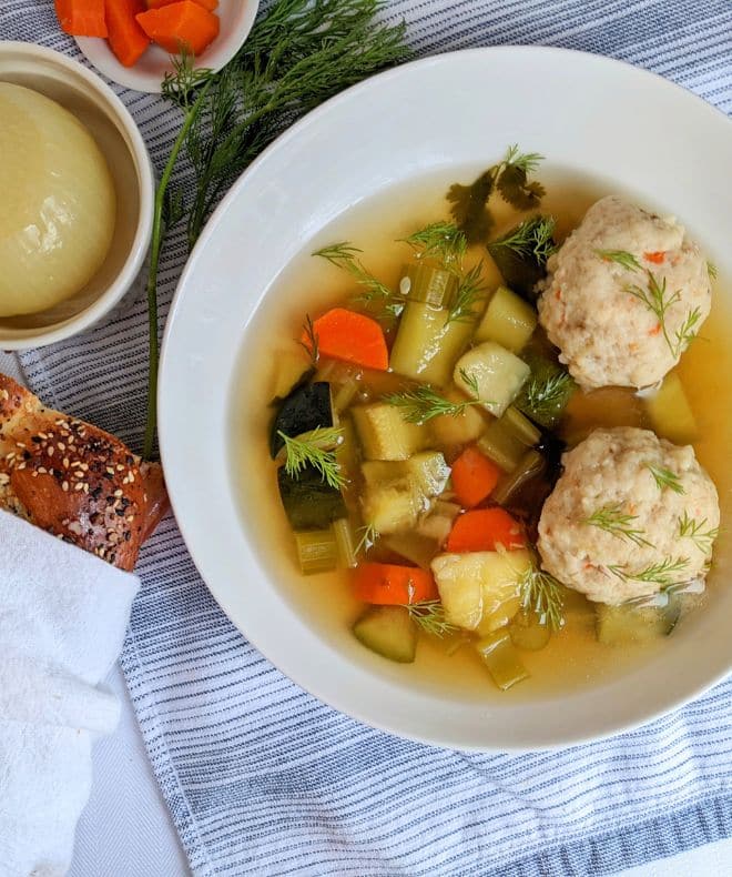 Vegetarian Matzo Ball Soup in a white bowl with bread on the side