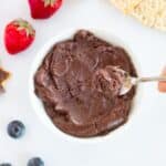 chocolate tahini spread in a white bowl and a teaspoon with the spread is on top