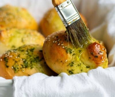 Garlic-Challah-Knots on in a white basket and a brush is spreading olive oil