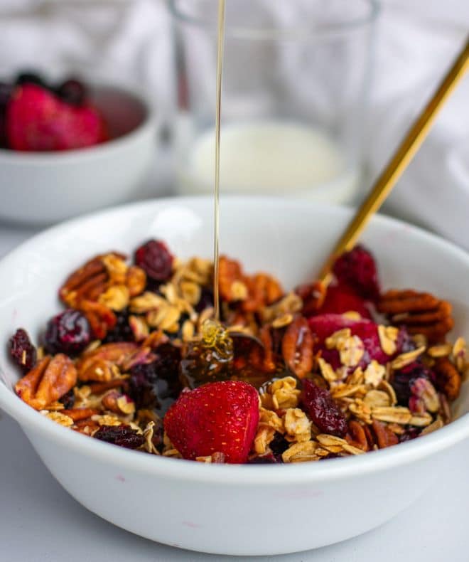 Maple Pecan Granola in a white bowl with honey