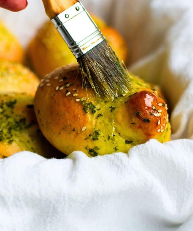Garlic-Challah-Knots on in a white basket and a brush is spreading olive oil