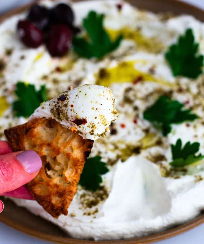 a hand holding a chips with Labneh with Garlic and Za’atar