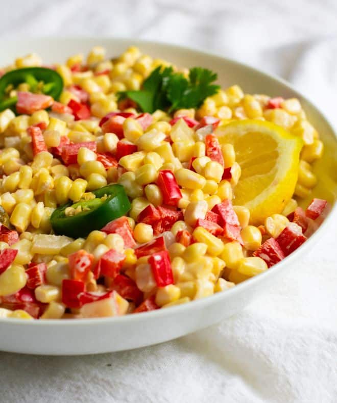 corn salad with tomatoes and lemon in a white bowl.
