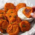 Sweet Potato Fritters on a white paper and a hand dipping in sauce