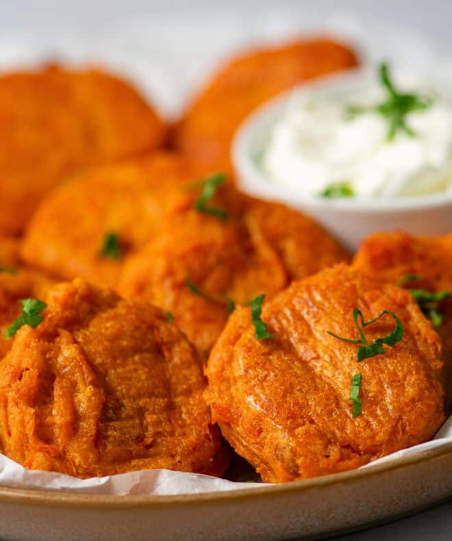 Sweet Potato Fritters on a white paper and a hand dipping in sauce