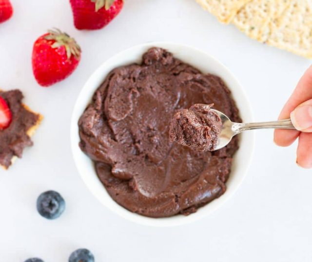 chocolate tahini spread in a white bowl and a teaspoon with the spread is on top